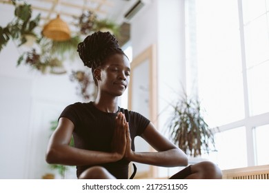 Calm and spiritual young interracial woman with hands holding together in namaste pose, sitting in lotus asana posture. Yoga Ardha Padmasana practicing at home. Relaxing and harmony on vacation. 