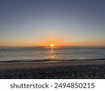 Calm sunrise over the ocean at South Beach, Miami Beach, Miami, Florida. The sun rises on the horizon, casting a golden glow across the sky and reflecting off the gentle waves. 