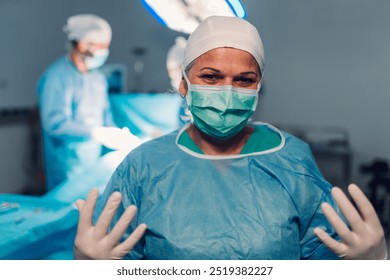 A calm surgeon is fully dressed in surgical attire, including a mask and gown, with colleagues performing surgery in the background under the bright surgical lights. - Powered by Shutterstock