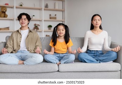 Calm Teen Girl, Millennial Korean Guy And Lady With Closed Eyes Sit On Sofa In Lotus Position, Practice Yoga In Living Room Interior. Relax Together, Sports And Peace At Home During Covid-19 Pandemic