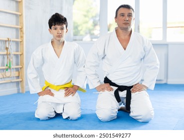 Calm teenage boy and middle-aged man wearing kimono sitting in seiza position in sports hall - Powered by Shutterstock