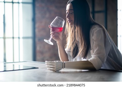 Calm Thoughtful Girl Holds Glass Of Wine In Bionic Arm At Home, Woman With Artificial Prosthetic Limb