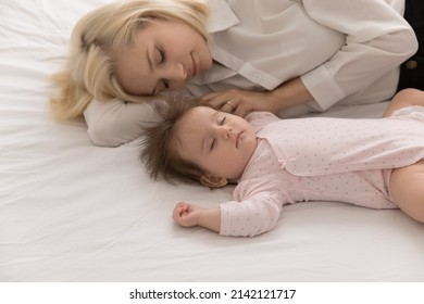 Calm Tired New Mom And Beautiful Infant Sleeping Together, Lying In Bed On White Linen Sheet, Relaxing In Bedroom, Taking Break, Pause. Young Mother Relaxing Near Sleepy Baby At Home. Motherhood