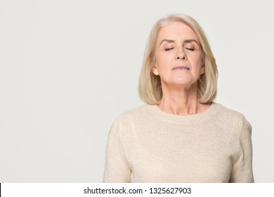 Calm Tranquil Mid Aged Old Woman Meditating Breathing Fresh Air, Serene Mindful Mature Senior Lady Taking Deep Breath Feeling No Stress Free Relief Harmony Isolated On White Grey Studio Background