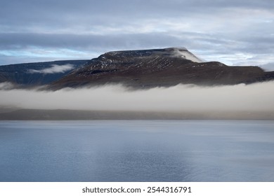 Calm water in a fjord. Mountains with a fog in the background. Cloudy sky during sunset. Akrafjall, Iceland. - Powered by Shutterstock