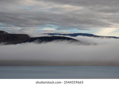 Calm water in a fjord. Mountains with a fog in the background. Cloudy sky during sunset. Akrafjall, Iceland. - Powered by Shutterstock