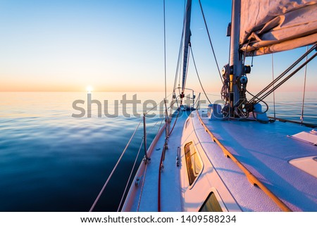 The calm water. White yacht sailing at sunset. A view from the deck to the bow, mast and the sails. Baltic Sea, Latvia