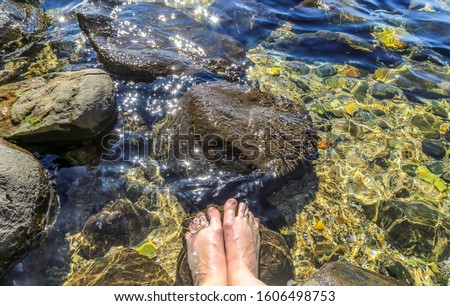 Calm water with a womens bare feet in a rock pool with bright sun reflecting on the water