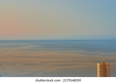 Calm waters during sunset with a hotel building overlooking the ocean. Aerial view of the sea during dusk. Copy space of small waves on calm water in the sea, bright afterglow in a clear summer sky - Powered by Shutterstock