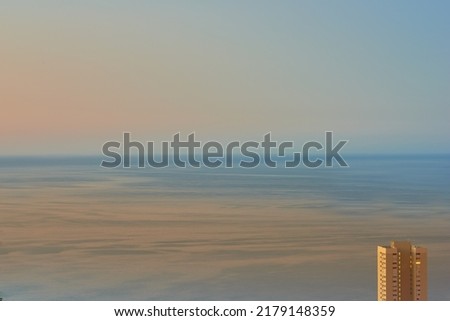 Calm waters during sunset with a hotel building overlooking the ocean. Aerial view of the sea during dusk. Copy space of small waves on calm water in the sea, bright afterglow in a clear summer sky