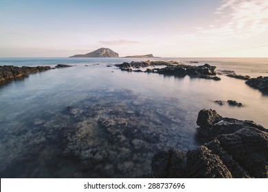 Calm waters of a tide pool off the east coast of Oahu, Hawaii during sunrise with two islands on the horizon