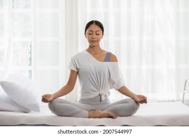 Calm of wellness Asian young woman sit on bed breathing with yoga lotus pose,Yoga meditation of young healthy woman relax and comfortable at white cozy home,Yoga Exercise for Wellness Concept - Shutterstock ID 2007544997