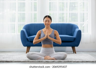 Calm of wellness Asian young woman sit on carpet breathing with yoga lotus pose,Yoga meditation of young healthy woman relax and comfortable at white cozy home,Yoga Exercise for Wellness Concept - Shutterstock ID 2069295437