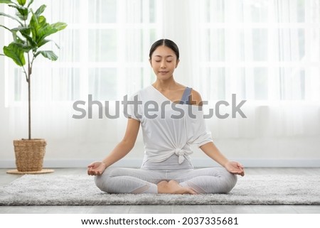 Calm of wellness Asian young woman sit on carpet breathing with yoga lotus pose,Yoga meditation of young healthy woman relax and comfortable at white cozy home,Yoga Exercise for Wellness Concept
