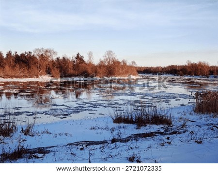 Calm Winter River with Thin Ice and Reflections. Serene river scene in winter with thin ice patches, reflections of bare trees, and clear sky overhead.