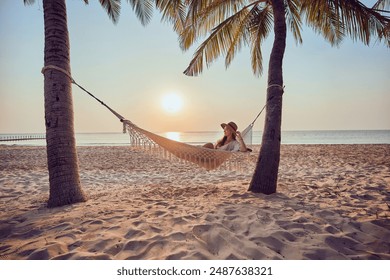 Calm woman with closed eyes chilling on a hammock on a tropical island among palm trees at sunset, enjoying relaxing and idyllic beautiful moment of life - Powered by Shutterstock