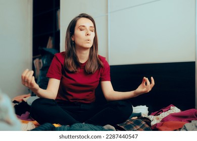 
Calm Woman Sitting in Yoga Pose on a Pile of Clothes. Professional organizer taking a deep breath before cleaning a closet
