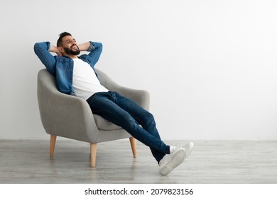 Calm young Arab man relaxing in armchair against white studio wall, copy space. Handsome middle Eastern guy enjoying peaceful weekend morning, resting with hands behind head - Shutterstock ID 2079823156