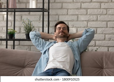 Calm young Caucasian man sit relax on sofa in living room take nap or sleep relieving negative emotions, happy millennial male rest on couch at home, breathe fresh air. Stress free, peace concept - Shutterstock ID 1800910525