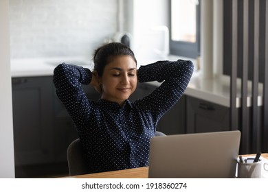 Calm young Indian woman sit at desk distracted form computer work sleep or doze off at workplace. Happy ethnic female relax at table in home office, relieve negative emotions. Stress free concept.