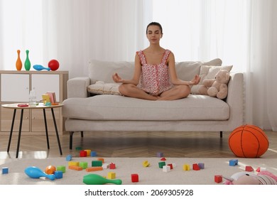 Calm Young Mother Meditating On Sofa In Messy Living Room