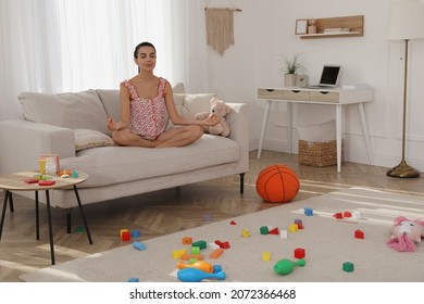 Calm Young Mother Meditating On Sofa In Messy Living Room