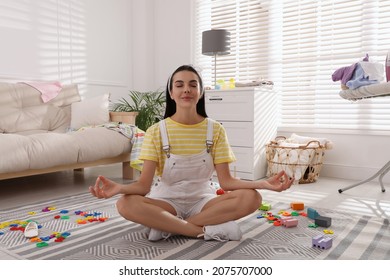 Calm Young Mother Meditating On Floor In Messy Living Room