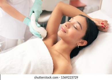 Calm young woman lying with closed eyes and putting on arm up while having laser hair removal procedure on it - Shutterstock ID 1369223729