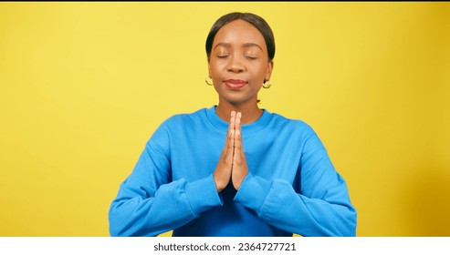 Calm young woman puts hands into prayer position, praying, yellow studio - Shutterstock ID 2364727721