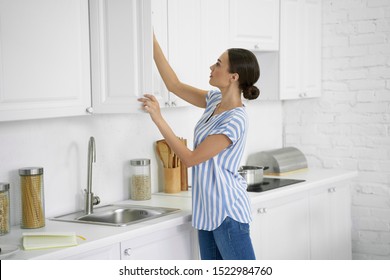 Calm young woman standing in the kitchen and taking food from the cupboard