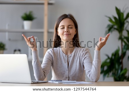 Calm young woman worker taking break doing yoga exercise at workplace, happy mindful female student meditating at home office desk feel balance harmony relaxation, stress relief zen at work concept
