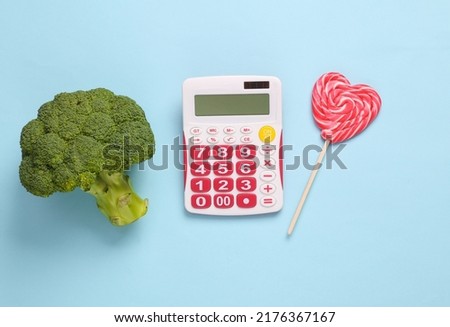 Calorie counting, weight loss concept. Calculator with broccoli and lollipop on blue background