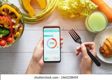 Calories counting , diet , food control and weight loss concept. woman using Calorie counter application on her smartphone at dining table with salad, fruit juice, bread and vegetable - Shutterstock ID 1465238459