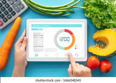 Calories Counting , Diet , Food Control And Weight Loss Concept. Woman Using Calorie Counter Application On Tablet At Dining Table With Fresh Vegetable And Calculator