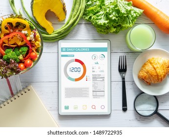 Calories Counting, Diet , Food Control And Weight Loss Concept. Tablet With Calorie Counter Application On Screen At Dining Table With Salad, Fruit Juice, Bread And Vegetable