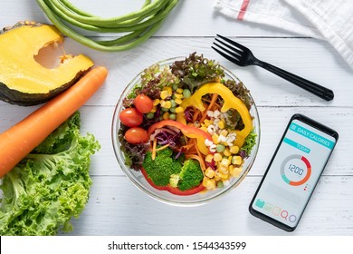 Calories Counting , Diet , Food Control And Weight Loss Concept. Calorie Counter Application On Smartphone Screen At Dining Table With Salad, Fruit Juice, Bread And Vegetable