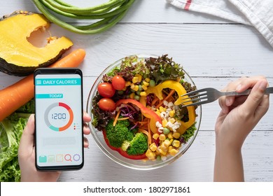 Calories counting , diet , food control and weight loss concept. Calorie counter application on smartphone screen at dining table with salad, fruit juice, bread and fresh vegetable. healthy eating - Shutterstock ID 1802971861