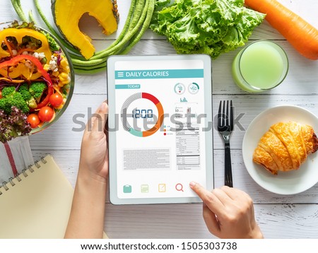 Calories counting , diet , food control and weight loss concept. woman using Calorie counter application on tablet at dining table with fresh vegetable salad