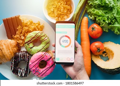 Calories counting and food control concept. woman using Calorie counter application on her smartphone with fresh vegetables, dessert and donuts on dining table - Shutterstock ID 1801586497
