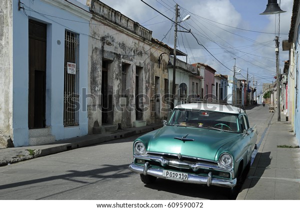 Camaguey, Cuba - 26 September, 2014: shinny vintage
green car parked on a narrow street, a display of typical Cuban
contrasts between old rundown houses in baroque architecture and
luxurious old cars