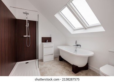 Cambridge, England - April 29 2019: Modern New Shower Room En Suite In White With Corner Walk In Cubicle, Bath Tub, Sink And Sloping Ceiling.