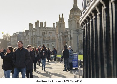 Cambridge, UK - Circa February 2020: Members of the public seen walking near a famous Cambridge University college in late winter. Part of the ornate wrought Iron fence and gothic architecture is seen
