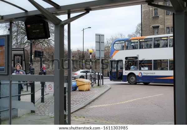 Cambridge, UK - Circa January 2020: Public double\
decker bus seen reversed from a bus station bay and making its way\
into busy city centre traffic. Members of the public can be seen\
around the station