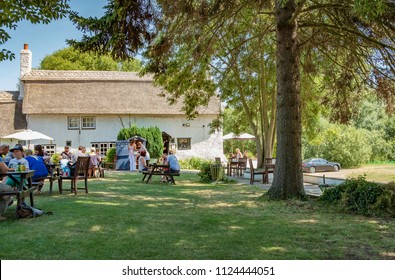 Cambridge, UK - Circa July 2018: Outdoor View Of A British Summer Beer Garden Next Adjacent To A Very Old, English Thatched Pub In Summer. The Foreground Shows Families Enjoying Refreshments.