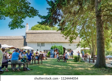 Cambridge, UK - Circa July 2018: Outdoor View Of A British Summer Beer Garden Next Adjacent To A Very Old, English Thatched Pub In Summer. The Foreground Shows Families Enjoying Refreshments.