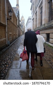 Cambridge UK December 2020 Rear View Of An Older Couple Walking Through The Senate House Passage Street In The Center Of Cambridge City On A Cold Rainy December Day