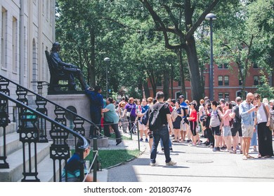 CAMBRIDGE, USA - JULY 14: View John Harvard Statue In Campus Of The Famous Harvard University In Cambridge, Massachusetts, USA With Some Students, Locals, And Tourists Passing By On July 14, 2019.