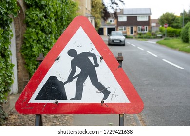 Cambridgeshire, UK - Circa May 2020: Close-up of a typical Roadworks sign seen located on a pavement area. A distant parked car is seen, major roadworks are nearby causing traffic issues.