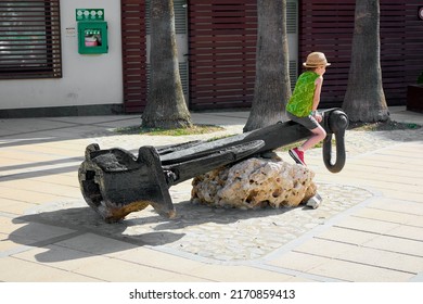 Cambrils, SPAIN - JUNE 24, 2022: Child Playing In The Olympic Port With An Anchor In The Context Of Having Vacations At School And Going For A Walk With His Parents Because He Is Bored At Home. 