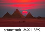 Camel caravan in front of the Great pyramid of Giza complex at red sunset - Cairo, Egypt